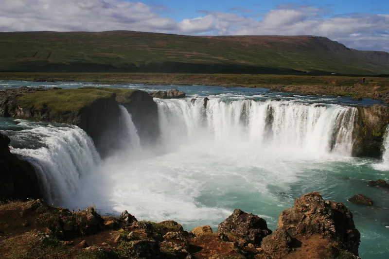 Der mächtige Wasserfall Godafoss in Island stürzt in einem weiten Bogen in ein türkisfarbenes Becken.