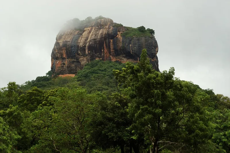 Der Sigiriya-Löwenfelsen in Sri Lanka ragt aus dem tropischen Regenwald empor und ist von Wolken umhüllt.