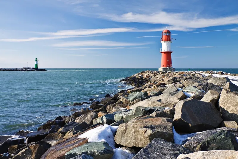 Zwei Leuchttürme an der Mole von Warnemünde im Winter mit Schnee auf den Felsen und ruhiger Ostsee.
